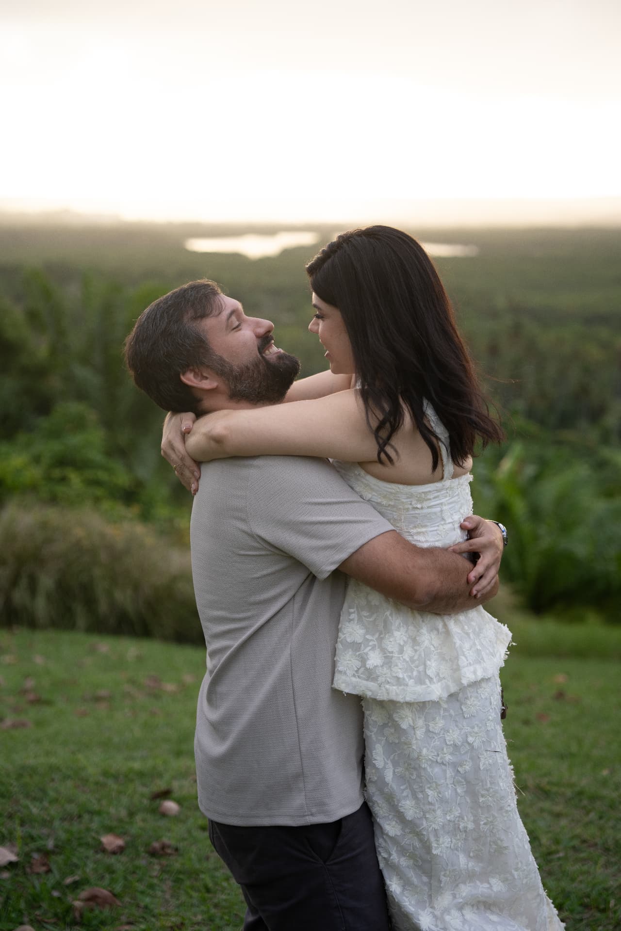 Lucas abraça Juliana pela cintura, rindo ao fim de tarde